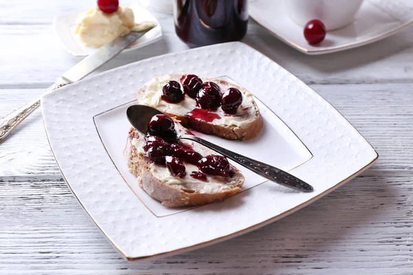 Pane fresco con marmellata di ciliegie e burro fatto in casa sul piatto sul tavolo di legno, su sfondo luminoso — Foto Stock