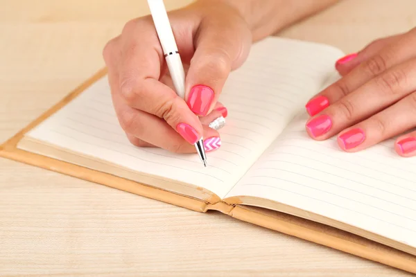 Vrouwelijke hand met stijlvolle kleurrijke nagels bedrijf pen, op houten tafel achtergrond — Stockfoto
