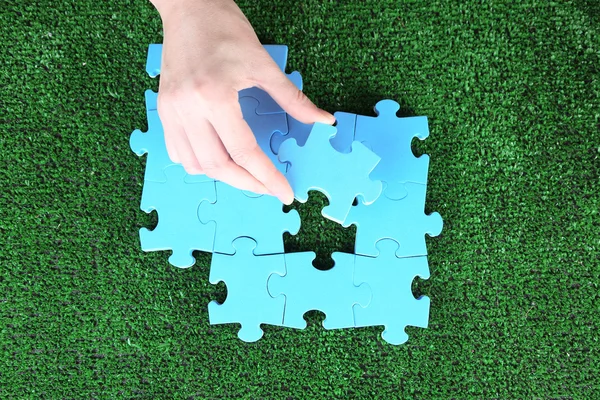 Tangan memegang potongan puzzle pada latar belakang rumput hijau — Stok Foto