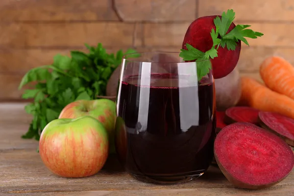 Glass of fresh beet juice and vegetables on wooden background