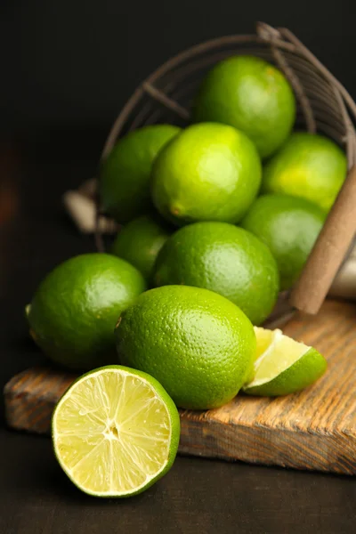 Fresh juicy limes in basket on wooden table, on dark background — Stock Photo, Image