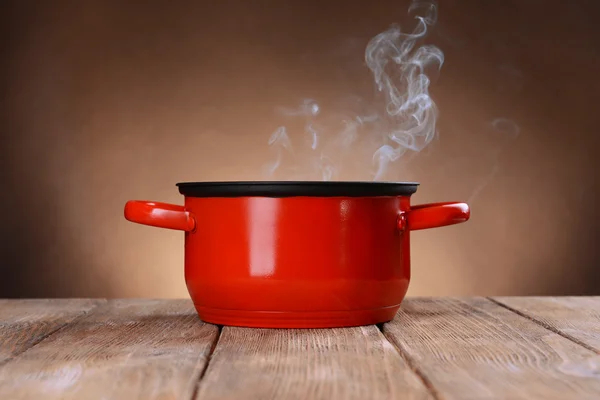 Kochtopf mit Dampf auf Tisch auf braunem Hintergrund — Stockfoto