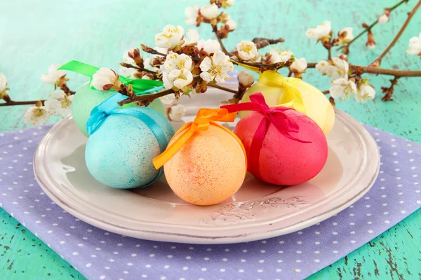 Uova di Pasqua su piatto con tovagliolo e fiori su tavolo di legno — Foto Stock