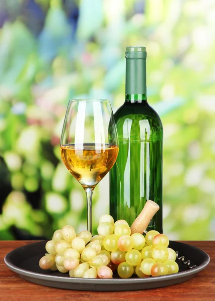 Fles wijn en een glas wijn op het dienblad, op lichte achtergrond — Stockfoto