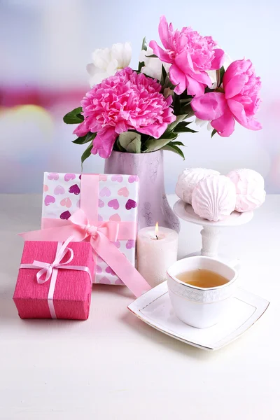 Composición de hermosas peonías en jarrón, té en taza y malvavisco, sobre mesa, sobre fondo claro —  Fotos de Stock