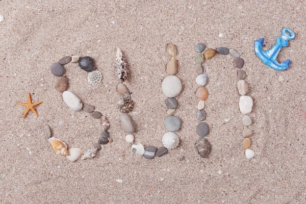 Palavra sol feito de conchas do mar e pedras na areia — Fotografia de Stock