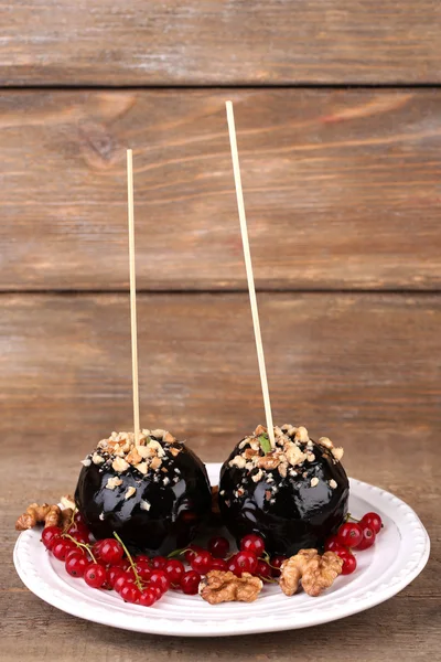 Sweet caramel apples on sticks with berries, on wooden table — Stock Photo, Image