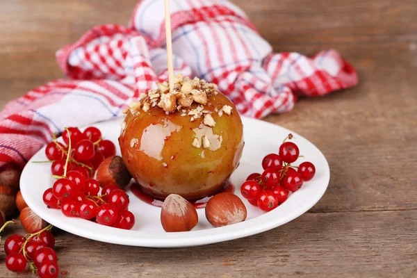 Mela caramellata dolce su bastone con bacche, su tavolo di legno — Foto Stock