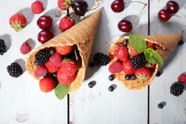 Beyaz ahşap zemin üzerinde şeker koni içinde farklı olgun çilek