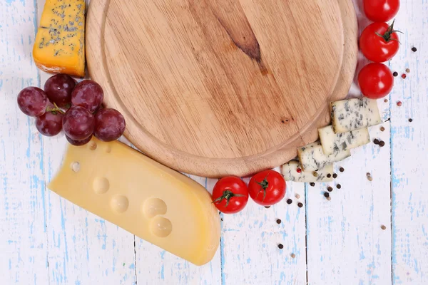 Different types of cheese with empty board on table close-up — Stock Photo, Image