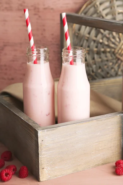 Botellas de sabrosas bebidas batido de frambuesa sobre fondo de madera rosa — Foto de Stock