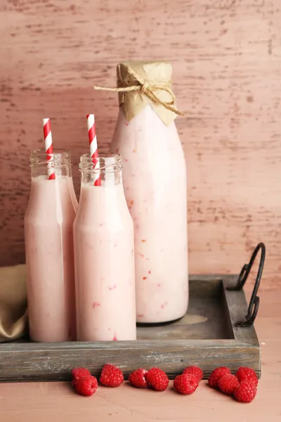 Botellas de sabrosas bebidas batido de frambuesa sobre fondo de madera rosa —  Fotos de Stock