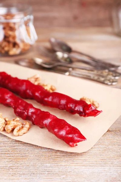 Tasty oriental sweets (churchkhela) and fresh nuts on paper, on wooden background — Stock Photo, Image