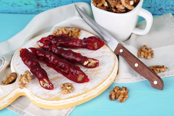 Sabrosos dulces orientales (churchkhela) y nueces frescas en la tabla de cortar, sobre fondo de madera — Foto de Stock