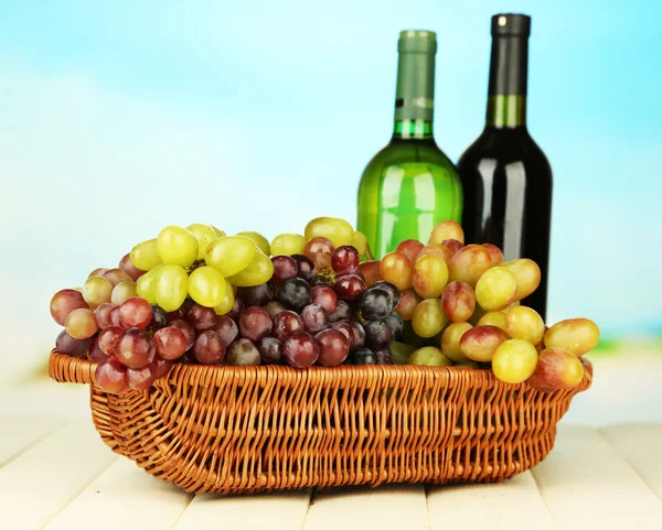 Uvas maduras en canasta de mimbre, botellas de vino, sobre fondo brillante — Foto de Stock