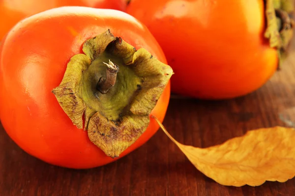 Ripe persimmons with yellow leaves on wooden background — Stock Photo, Image