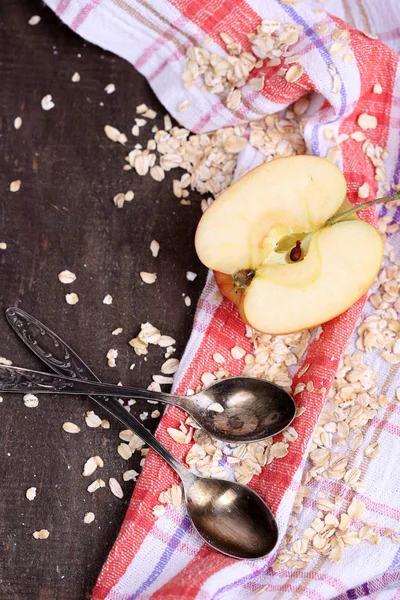 Mela con farina d'avena e cucchiai vintage su tovagliolo, su sfondo di legno a colori — Foto Stock