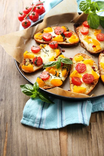 Tasty bruschetta with tomatoes on pan, on old wooden table — Stock Photo, Image