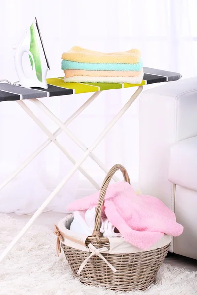 Baskets with laundry and ironing board on light home interior background — Stock Photo, Image