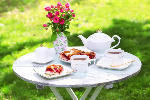 Salontafel met theekopjes en smakelijke taart in tuin — Stockfoto