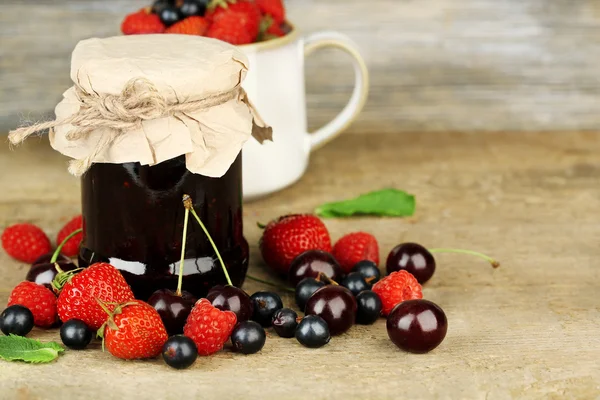 Tasty jam with berries in glass jar on wooden table — Stock Photo, Image