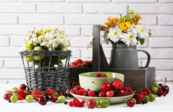 Still life with berries and flowers on white wall background