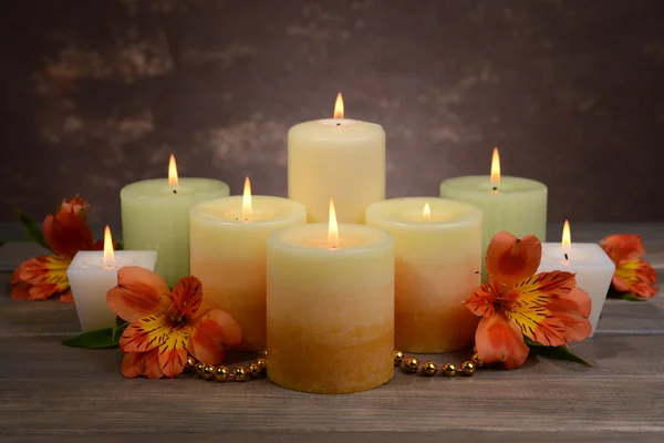 Mooie kaarsen met bloemen op tafel op bruine achtergrond — Stockfoto