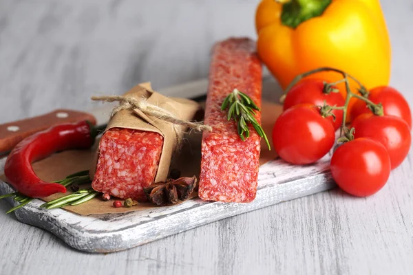 Sabrosa salchicha salami, verduras y especias sobre papel sobre fondo de madera —  Fotos de Stock