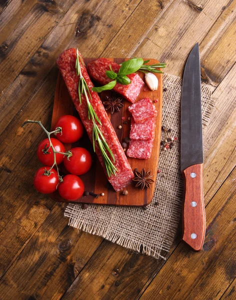 Leckere Salamiwurst und Gewürze auf Holzgrund — Stockfoto