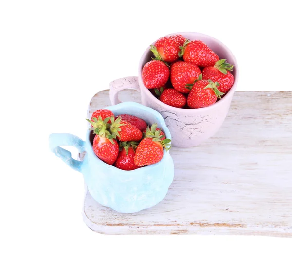 Ripe sweet strawberries in color mugs on cutting board isolated on white — Stock Photo, Image