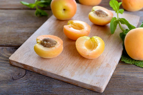 Ripe apricots with green mint leaves on cutting board, on wooden background — Stock Photo, Image