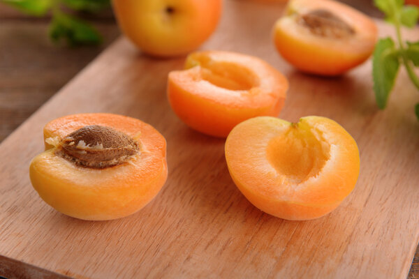 Ripe apricots with green mint leaves on cutting board, on wooden background
