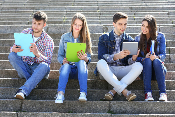 Happy students sitting on stairs in park