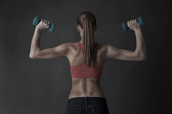 Joven hermosa chica de fitness haciendo ejercicio con pesas, sobre fondo gris —  Fotos de Stock