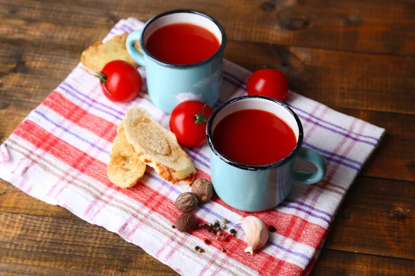 Domácí rajčatová šťáva v barevné hrnky, toasty a čerstvá rajčata na dřevěné pozadí — Stock fotografie