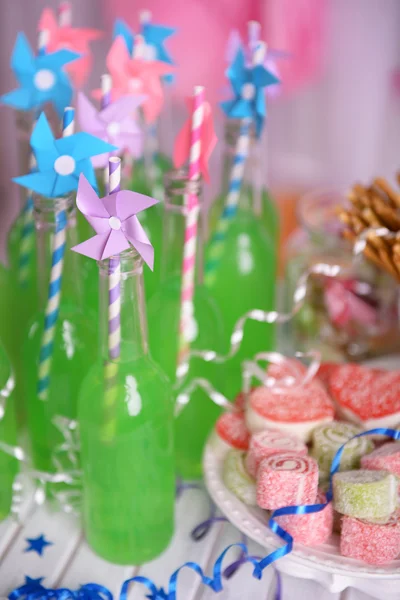 Garrafas de bebida com palha e doces em fundo decorativo — Fotografia de Stock