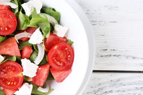 Salade avec melon d'eau, oignon, roquette et feuilles d'épinards sur assiette, sur fond de bois — Photo