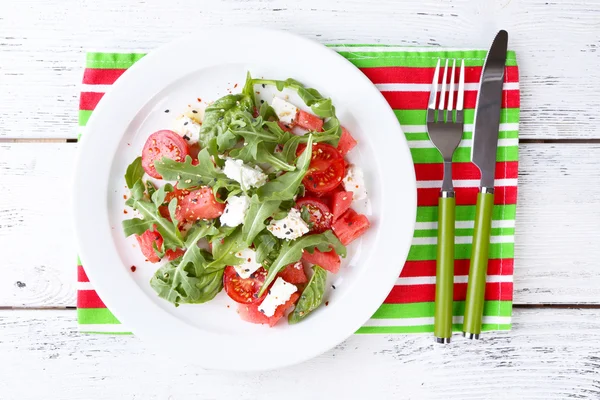 Salada com melancia, tomates, feta, rúcula e manjericão folhas no prato, no fundo de madeira — Fotografia de Stock