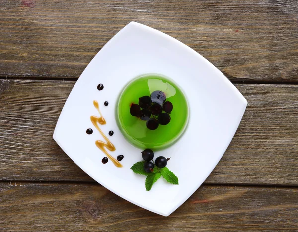 Jalea verde con bayas de grosella negra y salsa, sobre fondo de madera — Foto de Stock