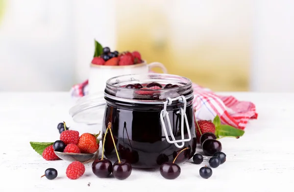 Tasty jam with berries in glass jar on wooden table — Stock Photo, Image