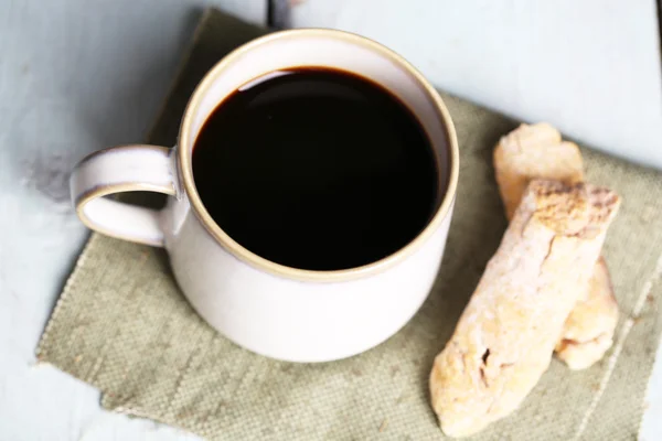 Tasse mit heißem Kaffee und gerösteten Kaffeekörnern auf Serviette, auf Holztischhintergrund — Stockfoto