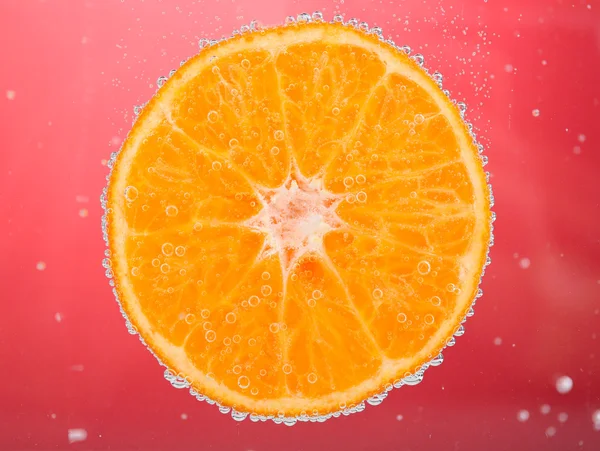 Fresh orange in water with bubbles on red background — Stock Photo, Image