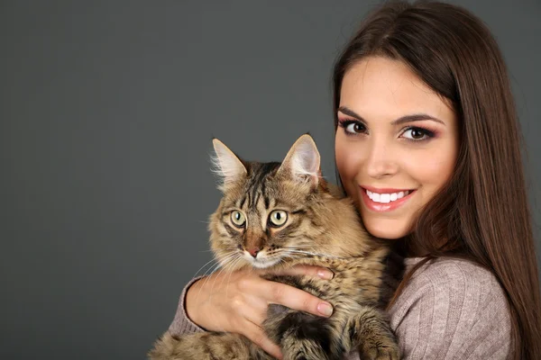 Hermosa mujer joven sosteniendo gato sobre fondo gris — Foto de Stock