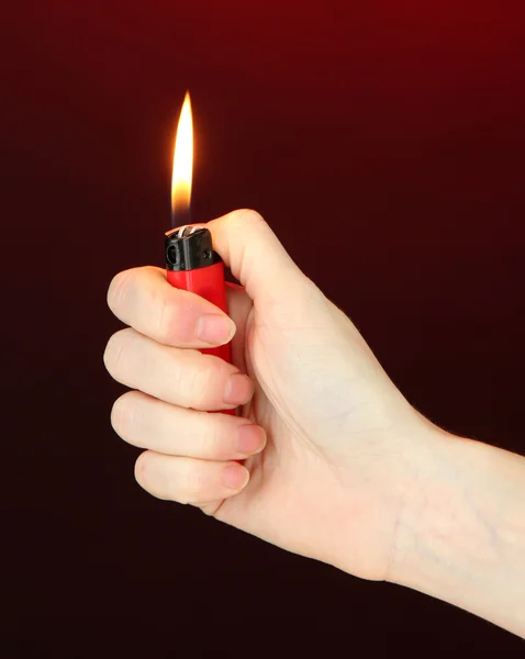 Acendedor em chamas na mão feminina, no fundo vermelho escuro — Fotografia de Stock