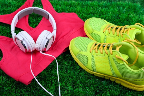 Sport clothes, shoes and headphones on green grass background