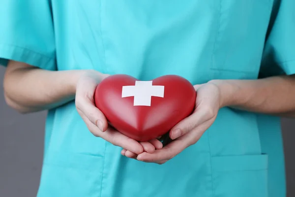 Coeur rouge avec signe de croix dans la main du médecin — Photo