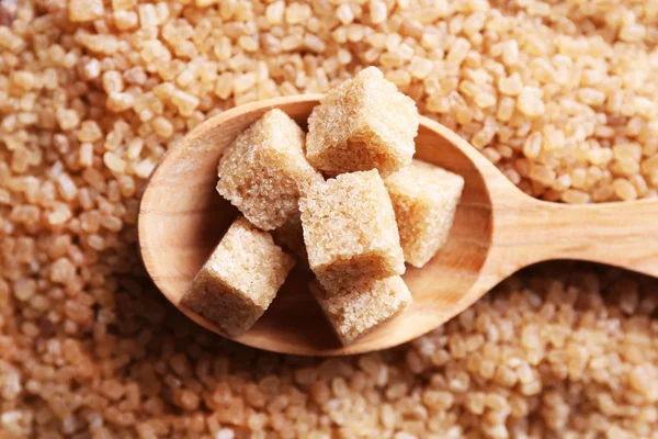 Brown sugar cubes in wooden spoon on crystal sugar background — Stock Photo, Image