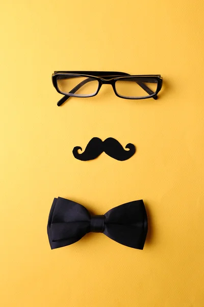 Glasses, mustache and bow tie forming man face on yellow background — Stock Photo, Image