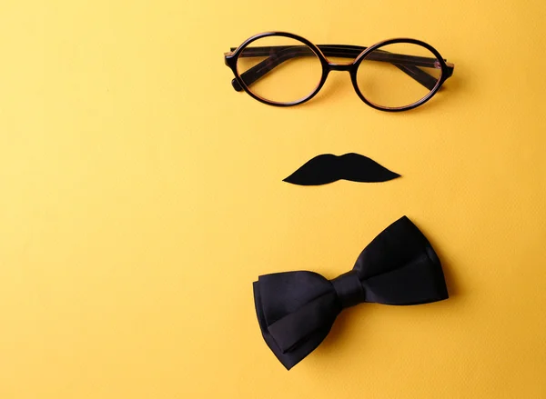Glasses, mustache and bow tie forming man face on yellow background — Stock Photo, Image