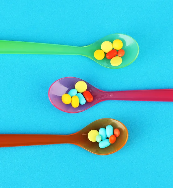 Cucharas de plástico con píldoras de color sobre fondo azul — Foto de Stock